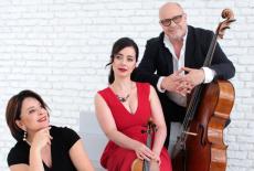 The trio poses together in front of a white brick wall, 2 dressed in black, 1 in a red dress